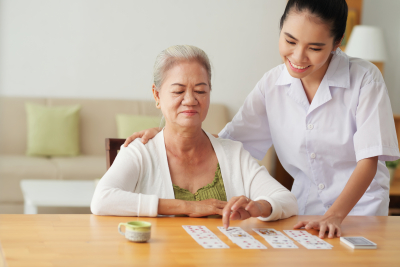 senior woman playing cards under supervision of her caregiver