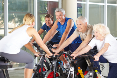 senior people with trainer in gym exercising on spinning bikes